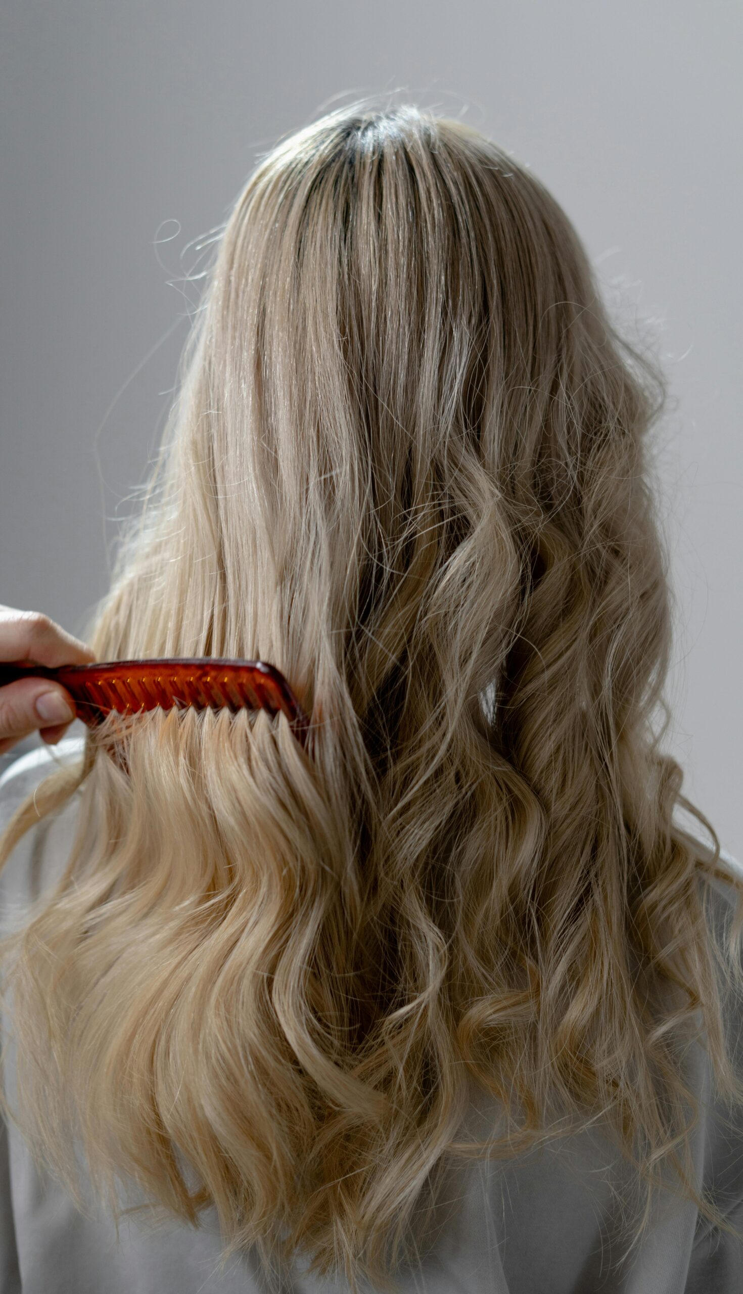 Back view of long blonde hair being combed into smooth curls with a red comb.